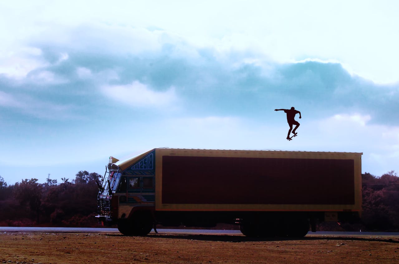 Dramatic shot of skateboarder mid-air atop a truck against a cloudy sky.